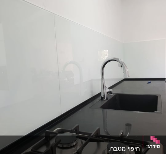 זכוכית שקופה על קיר מטבח מעל כיור וברז